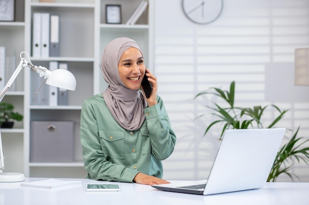 Smiling young muslim woman wearing hijab engaged in a pleasant conversation on her smartphone at