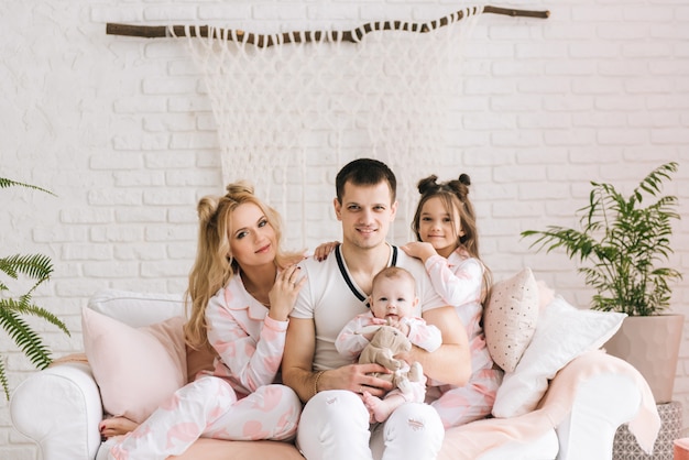 Smiling young parents and their two children are very happy, they are at home on the bright interior