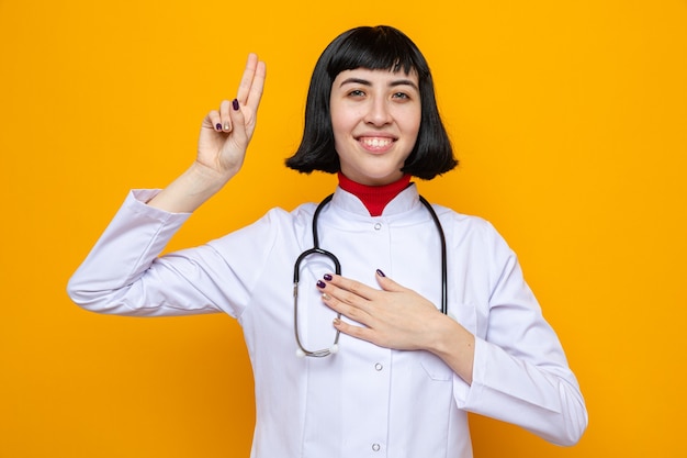 Smiling young pretty caucasian girl in doctor uniform with stethoscope making oath