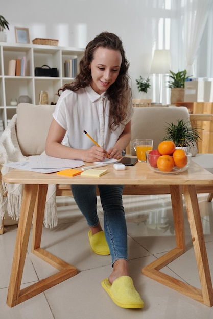 Smiling young project manager working from home writing down ideas working with documents and answer...