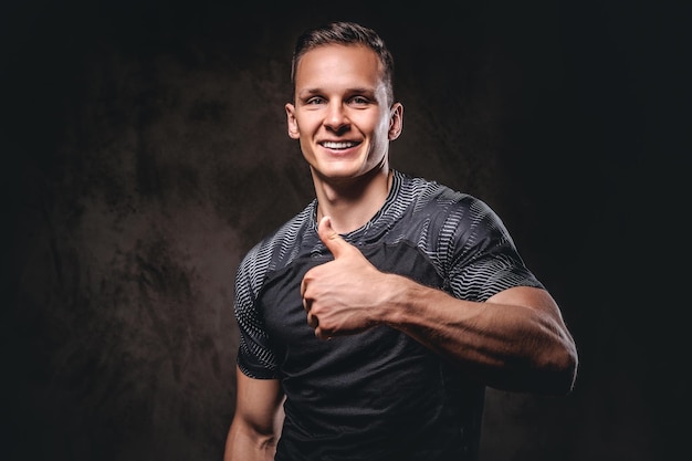 Smiling young sportsman showing thumbs up on a dark background.