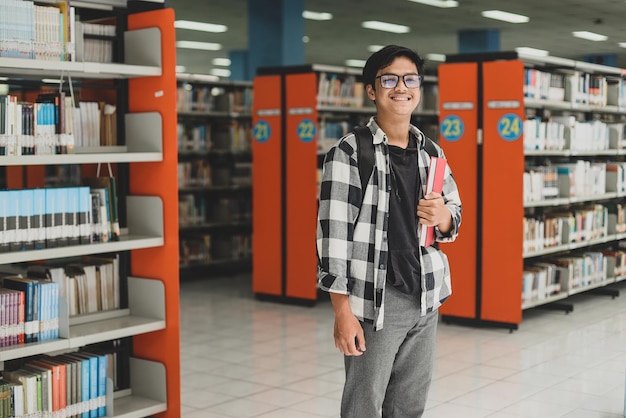 Smiling young student in casual style standing confidently while holding a book in the library