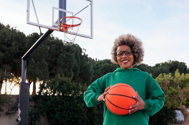 Smiling young woman on a basketball court holding a ball in his hands concept of urban sport in the street copy space for text