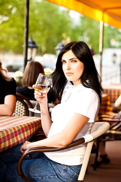 Smiling young woman at cafe drinking white wine. Communication and friendship concept.