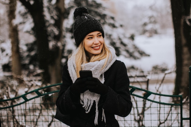 Smiling Young Woman in Cozy Clothing using mobile phone on winter day