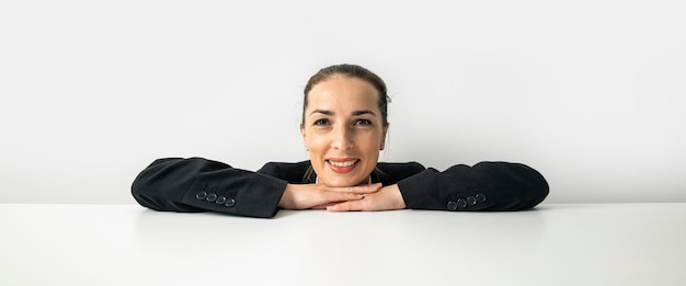 Smiling young woman folded her hands peeking out from behind white cardboard on white background Banner