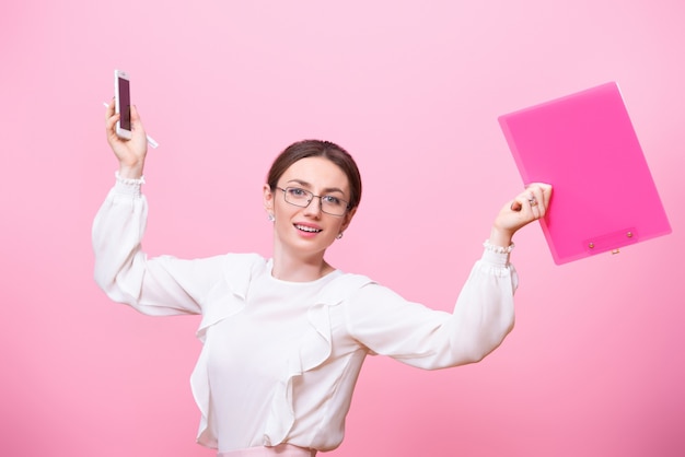 Smiling young woman in glasses holds a folder and a mobile phone in her hands