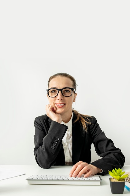 Smiling young woman in glasses with keyboard sitting at table at workplace