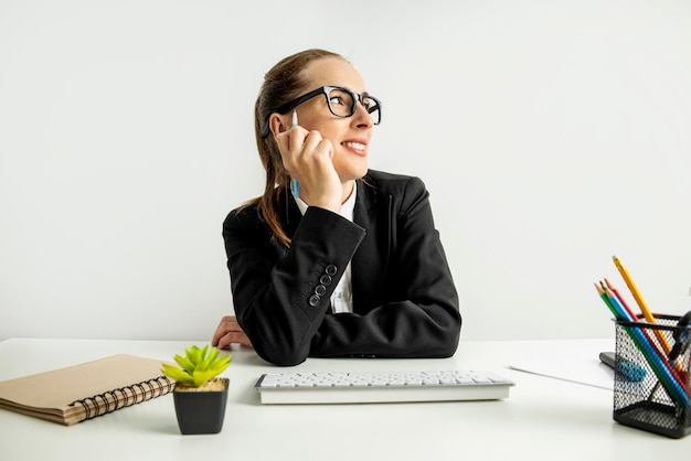 Smiling young woman in glasses with keyboard sitting at workplace