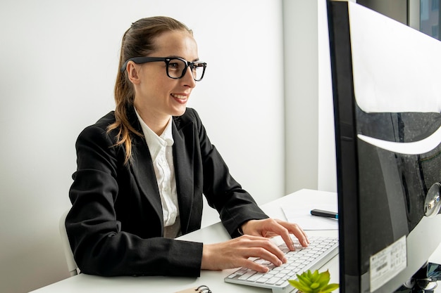 Smiling young woman in glasses works while sitting at a computer in the workplace