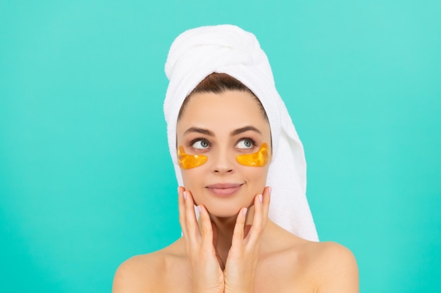 Smiling young woman has collagen golden eye patches on face with towel