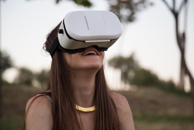 Smiling young woman having fun while using glasses of virtual reality in park.  