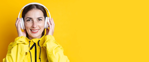 Smiling young woman in headphones in a yellow jacket on a yellow background Banner