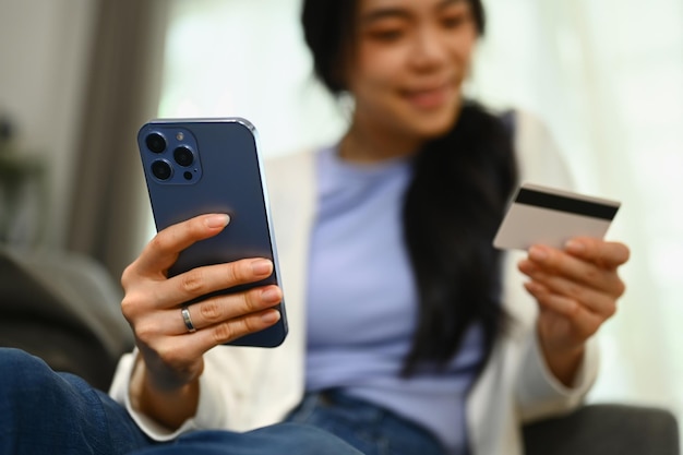 Smiling young woman holding credit cad and using smartphone for online banking transaction Selected focus on hand