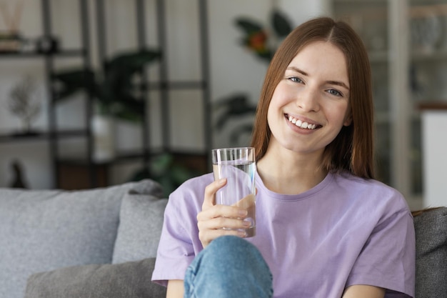 Smiling young woman holding a glass of clean water looking at the camera and smiling. Healthy lifestyle concept