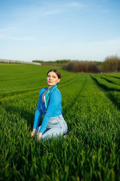 A smiling young woman is sitting in a spacious field on green grass