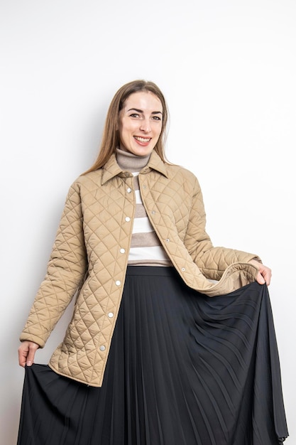 Smiling young woman in a jacket midi skirt against a white wall