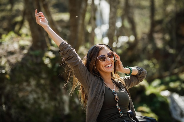 A smiling young woman listening music on her headphones while enjoying the outdoors.