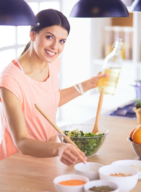 Smiling young woman mixing fresh salad in the kitchen