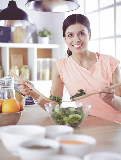 Smiling young woman mixing fresh salad in the kitchen