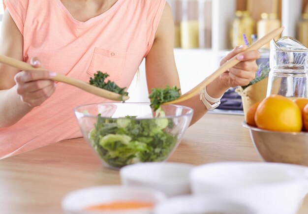 Smiling young woman mixing fresh salad in the kitchen