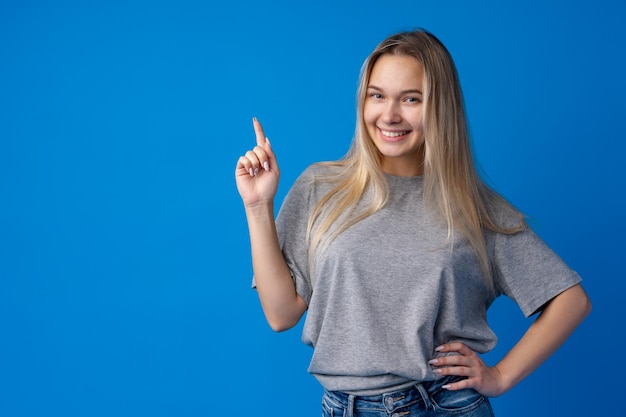 Smiling young woman pointing at copy space over blue background