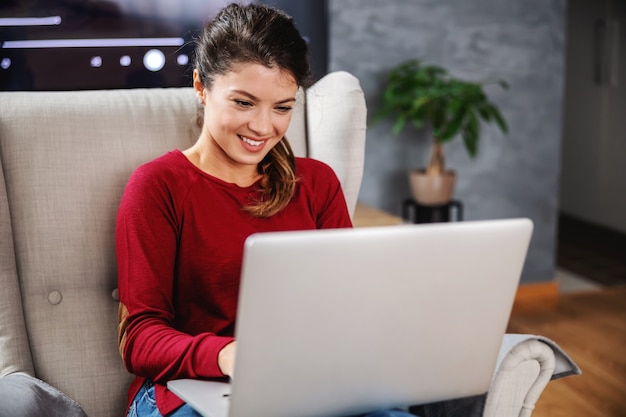 Smiling young woman sitting at home and using laptop.