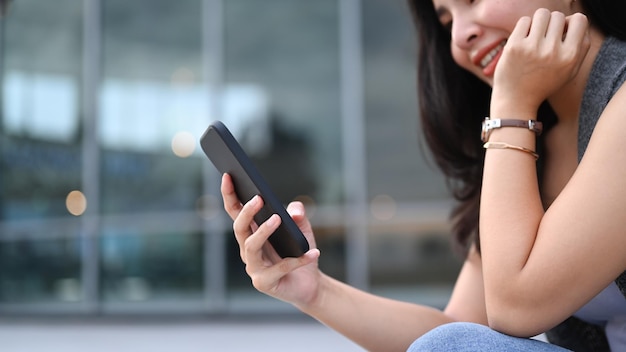 Smiling young woman sitting on the stairs outdoors and using smart phone