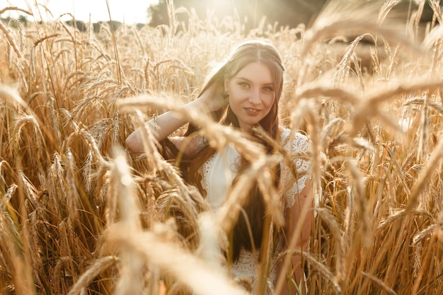 Smiling young woman standing in golden wheat field in summer and looking at camera 