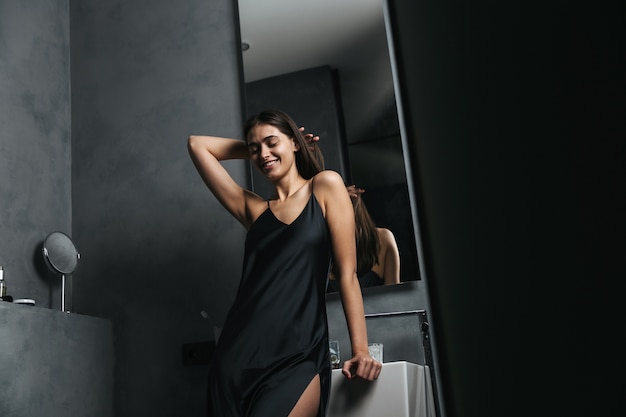 Smiling young woman standing at the mirror at the bathroom in the morning