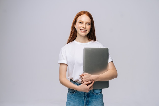 Smiling young woman student holding laptop computer and looking at camera on isolated background