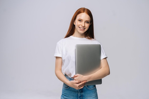 Smiling young woman student holding laptop computer and looking at camera on isolated background