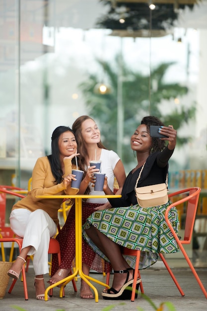 Smiling young woman taking selfie with her best friends when they are spending time in outdoor cafe