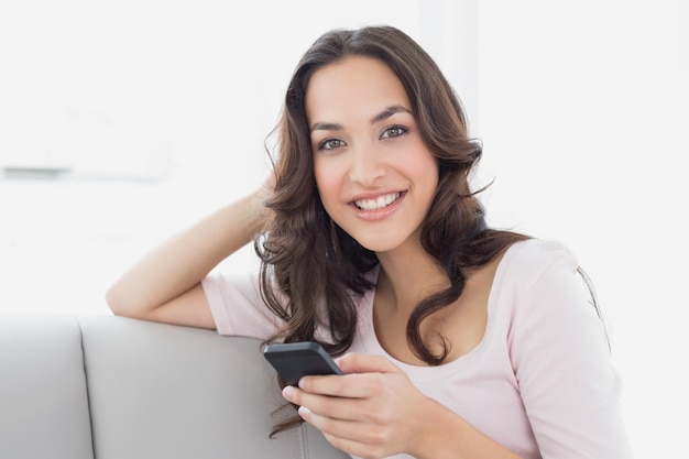 Smiling young woman text messaging on sofa at home