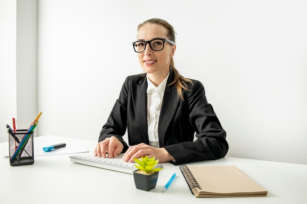 Smiling young woman typing on keyboard while sitting at desk at workplace