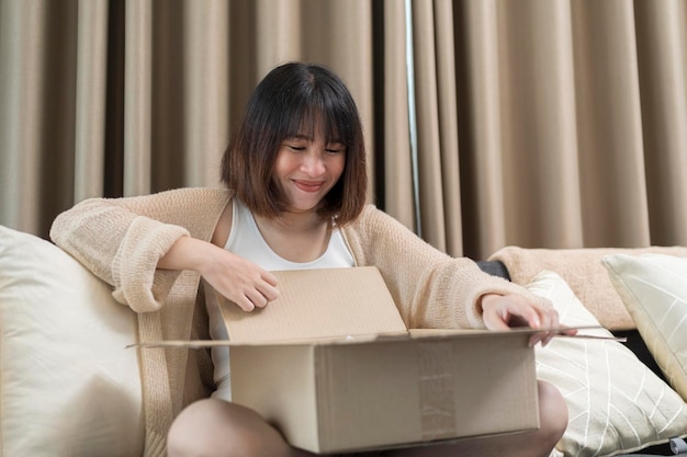 Smiling young woman unpacking parcel sitting on couch at home pretty curious girl opening cardboard box close up satisfied client received online store order