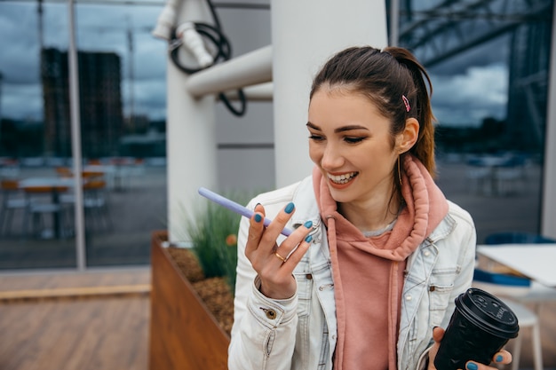 Smiling young woman  use smartphone to take a taxi after shopping and holding coffee cup, grocery shopping paper bag with long white bread baguette