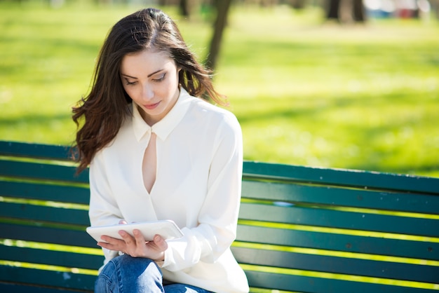 Smiling young woman using her tablet in a park