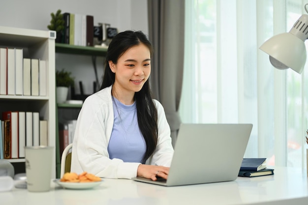 Smiling young woman using laptop at home sending email or browsing internet People and technology concept