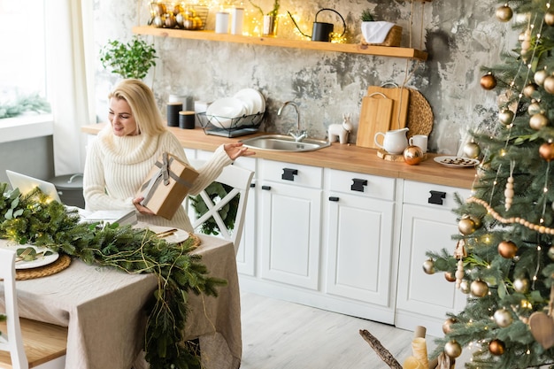 Smiling young woman using laptop near christmas tree.