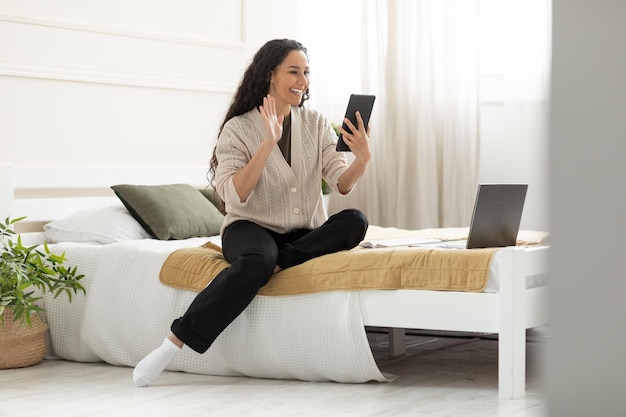 Smiling young woman waving hand using digital tablet