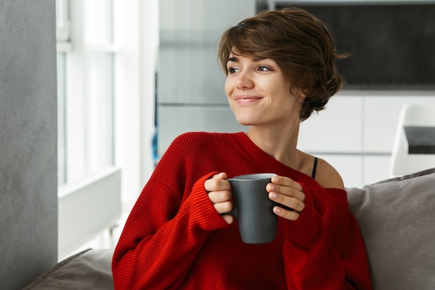 Smiling young woman wearing sweater relaxing on a couch at home