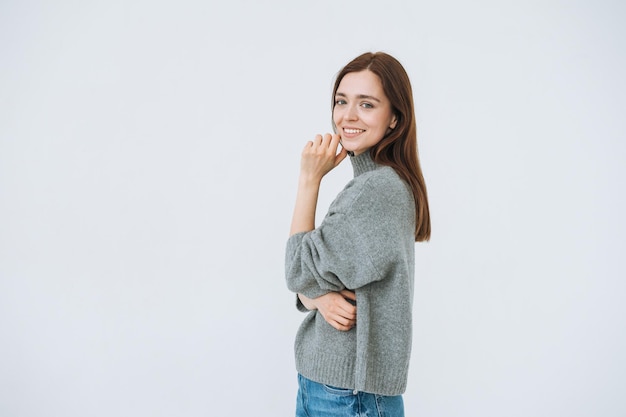 Smiling young woman with dark long hair in grey knitted swaeter on the white background isolated