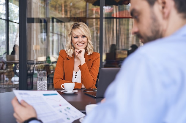 Smiling young woman with her chin propped on her hand staring at her male colleague