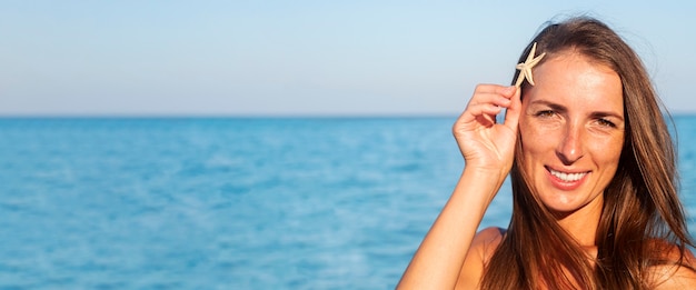 Smiling young woman with starfish on the background of the sea. Banner.