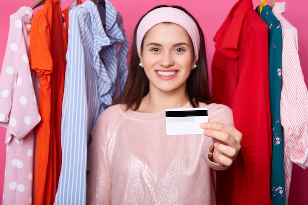 Smiling yuong dark haired woman holds credit card.