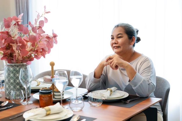 Smilling asian older woman waiting breakfast food by sitting at dinning table at home