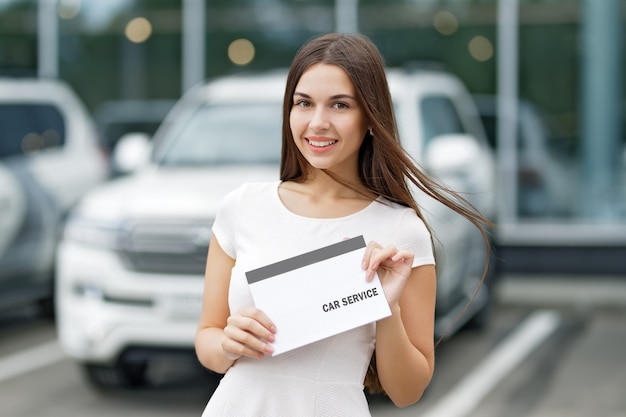 Smilling woman with agreement car service on background of dealership