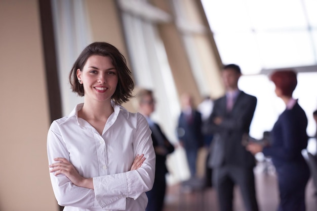 Smilling young business woman in front her team blured in background. Group of young business people. Modern bright  startup office interior.