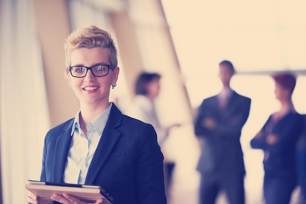 Photo smilling young business woman with tablet computer  in front her team blured in background. group of young business people. modern bright  startup office interior.